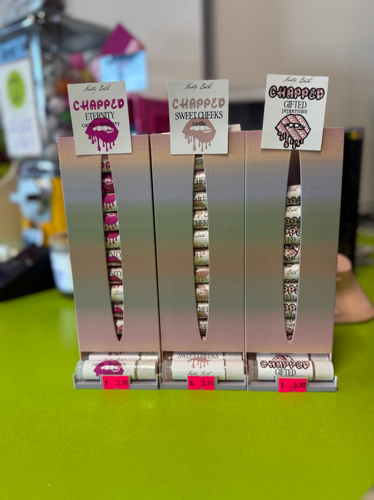 Set of lip glosses in a display stand with 'Chapped' branding on a green surface.