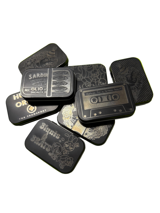 A Stack of matte black aluminum storage tins with various images laser engraved on them